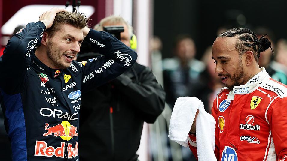 Max Verstappen and Lewis Hamilton engage with each other at the end of the Canadian Grand Prix, with Verstappen holding his hands over his head and Hamilton holding a white towel as both wear their racing suits