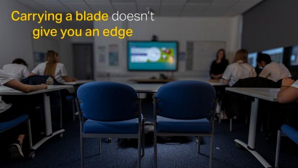 Photo of school room with words in the corner in yellow and white, saying: "Carrying a blade doesn't give you an edge"