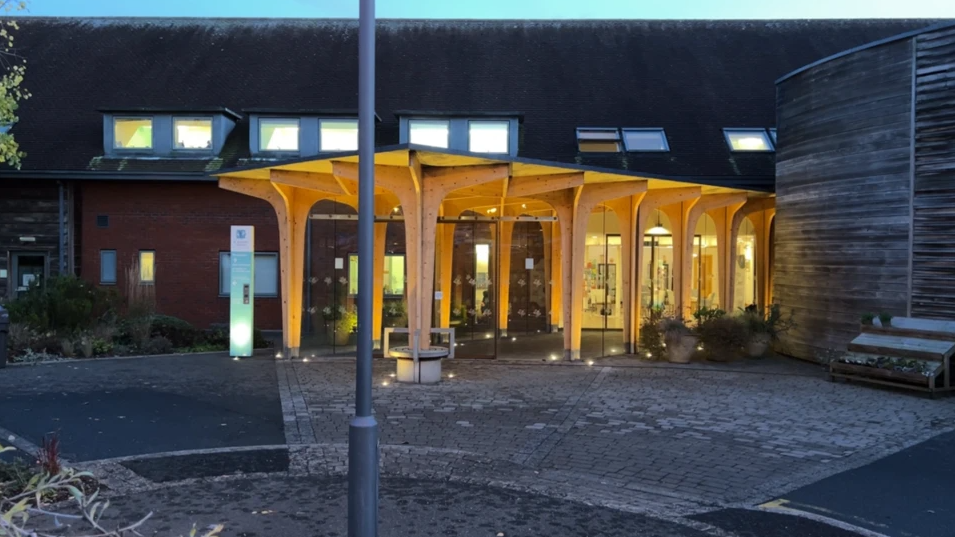 The outside of the hospice is lit up. The building  has wooden panelling and a large concrete front area.