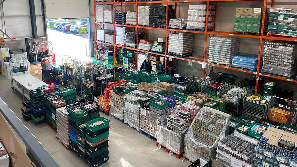 Warehouse containing rows of food items on pallets and in crates for a food bank charity 