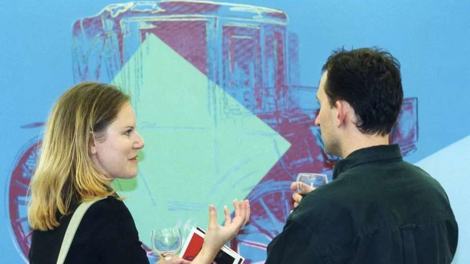 Two people holding wine glasses in front of an Andy Warhol piece of art at MK Gallery in 2001