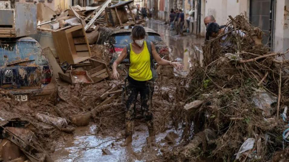 A woman walks along a street full of mud and waste from houses after heavy rain and flooding.