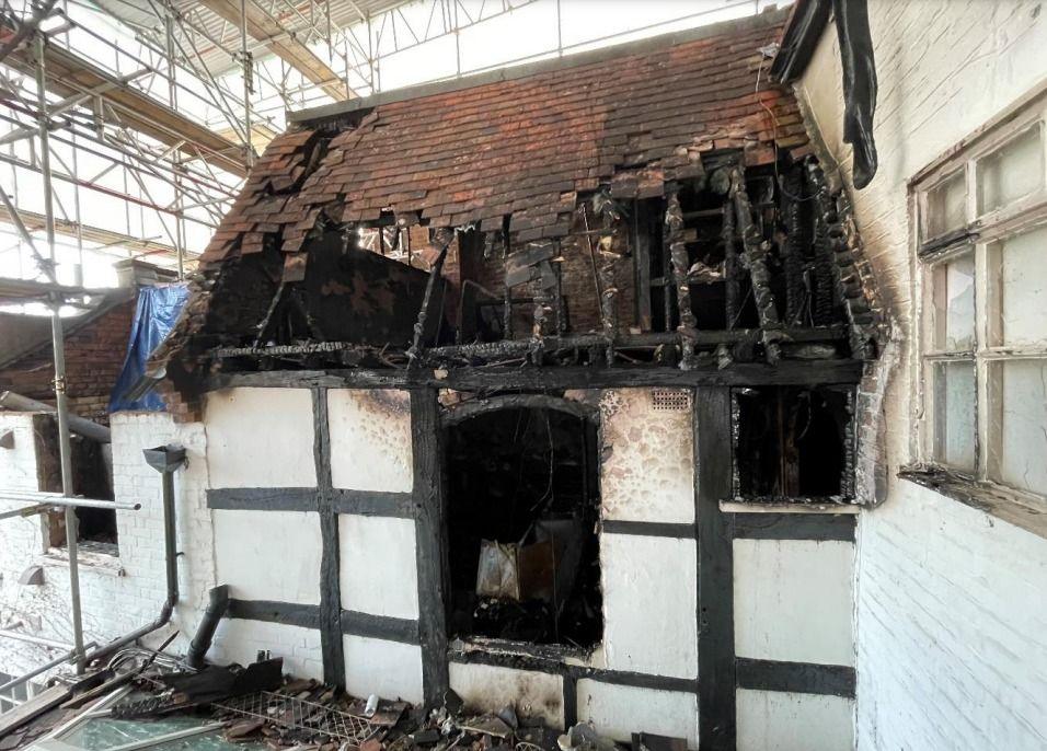 Fire-damaged section of a black and white building with burnt timbers and collapsed roof