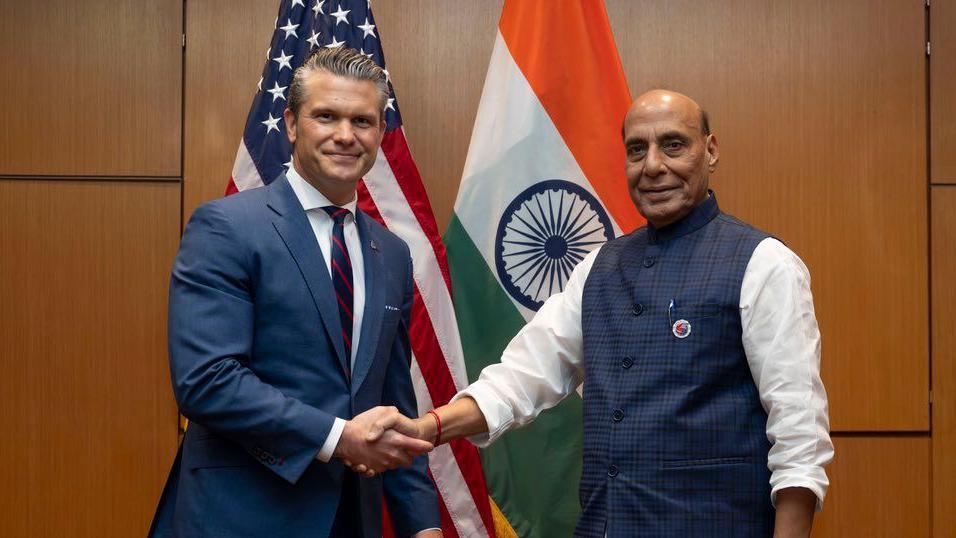 US Defence Secretary Pete Hegseth (L) and India's Defence Minister Rajnath Singh shake hands after meeting in Kuala Lumpur, with their countries flags behind them.