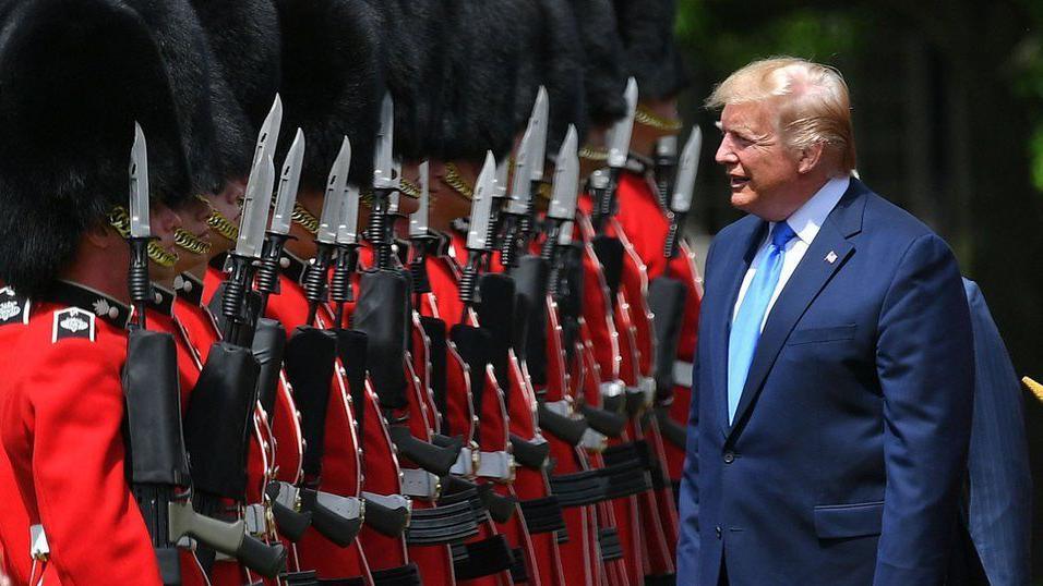 Wearing a blue suit and pale blue tie, Donald Trump inspects a Guard of Honour formed by red-coated Grenadier Guards at Buckingham Palace during his state visit to the UK in June 2019.