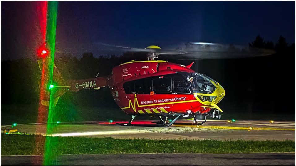 A red helicopter with yellow trim on a helipad at night with green and red lights on its tail shining