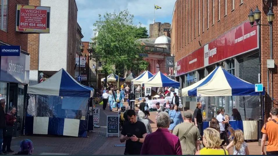 A busy street market with dozens of people looking at stalls