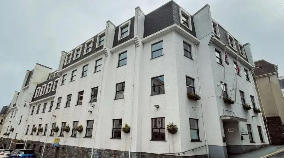 A four-storey white building on a corner block under a cloudy sky.