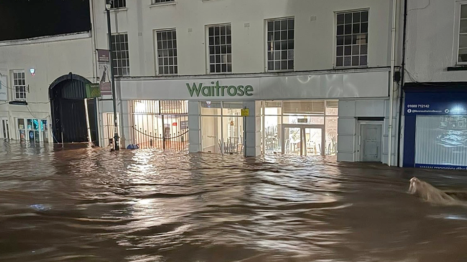 Water can be seen inside a store as it pours along a main street in Monmouth. The white building has a sign which reads Waitrose in green font. Kim Kaos