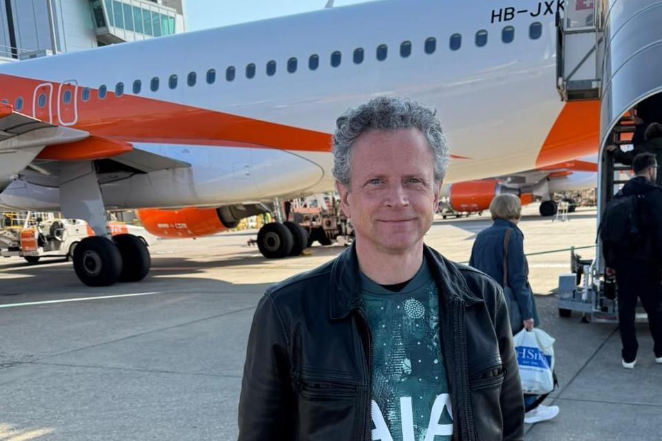 Michael Green wearing a bluey-green Spurs on the runway in front of an orange and white plane