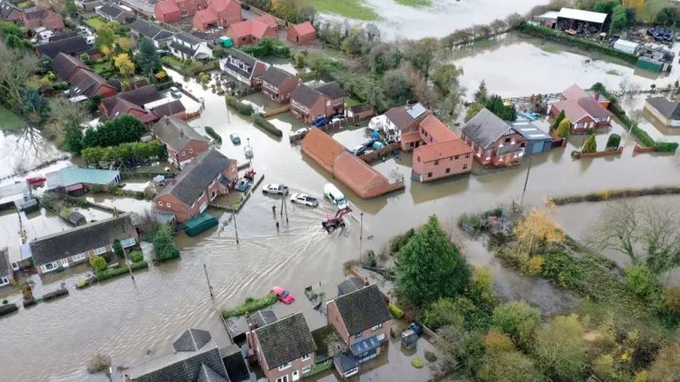 An aerial view of the village of Fishlake when it was flooded in 2019, showing houses and trees surrounded by water and cars afloat nearby 