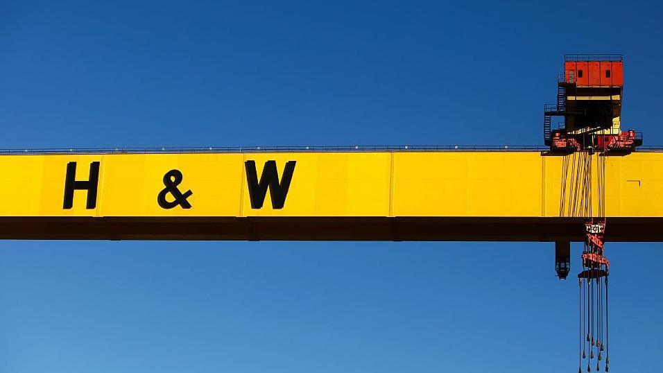 A crane silhouetted against a blue sky. The crane spans the width of the frame and on the side in large black letters is written H & W.