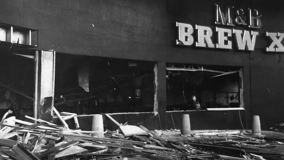 A black and white photo of the aftermath of the explosion at one pub. Debris and glass can be seen on the floor with a sign of M&B Brew XI on the building
