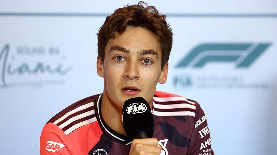 George Russell holds a microphone 