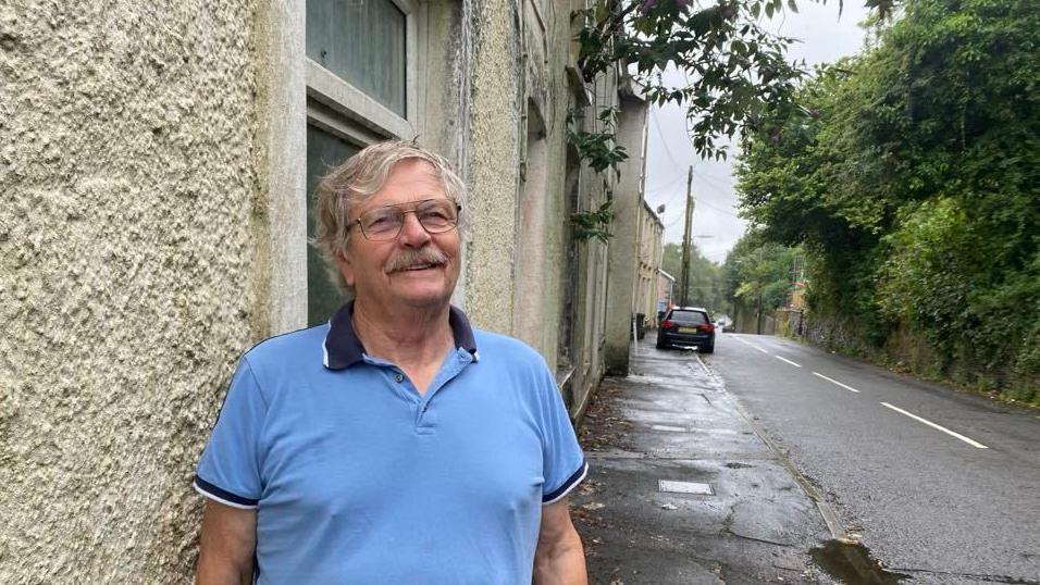 Gabe Thomas, in a blue shirt, standing outside one of the houses in Cyfyng Road