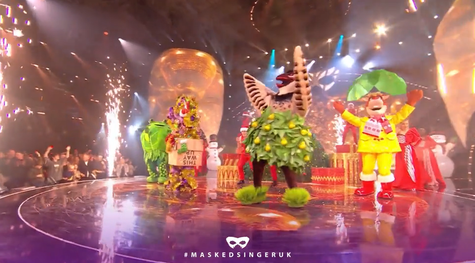 Still from the Masked Singer Christmas special showing people on stage in festive costumes including a sprout, a Christmas tree and a turkey,