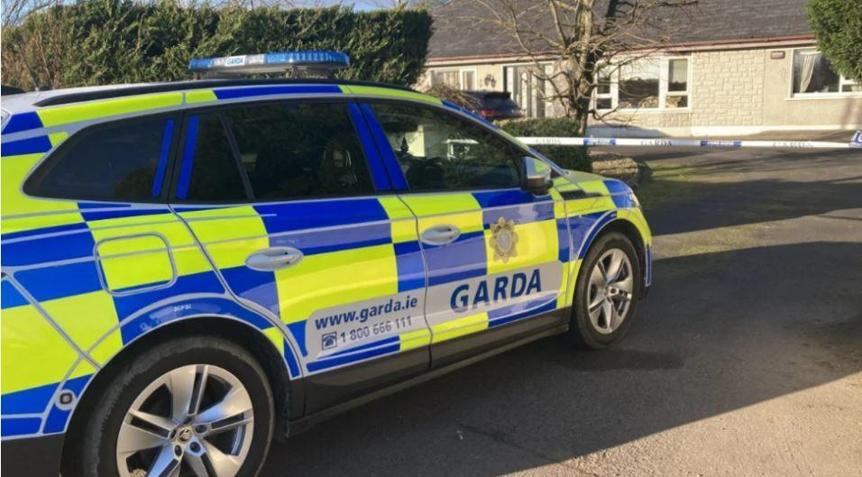 A garda car parked outside of a house with a police cordon visible 