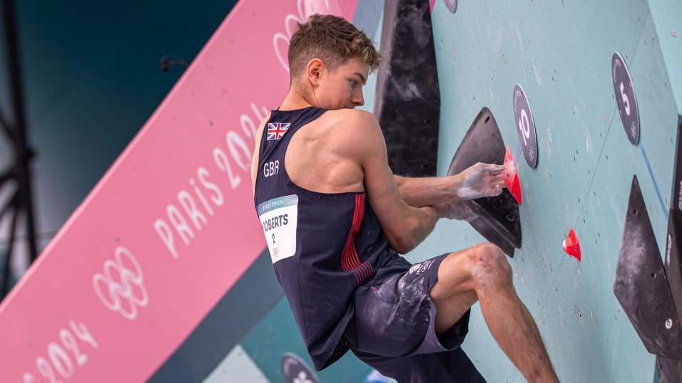 A TeamGB athlete climbs up a wall at the Paris Olympics 2024.