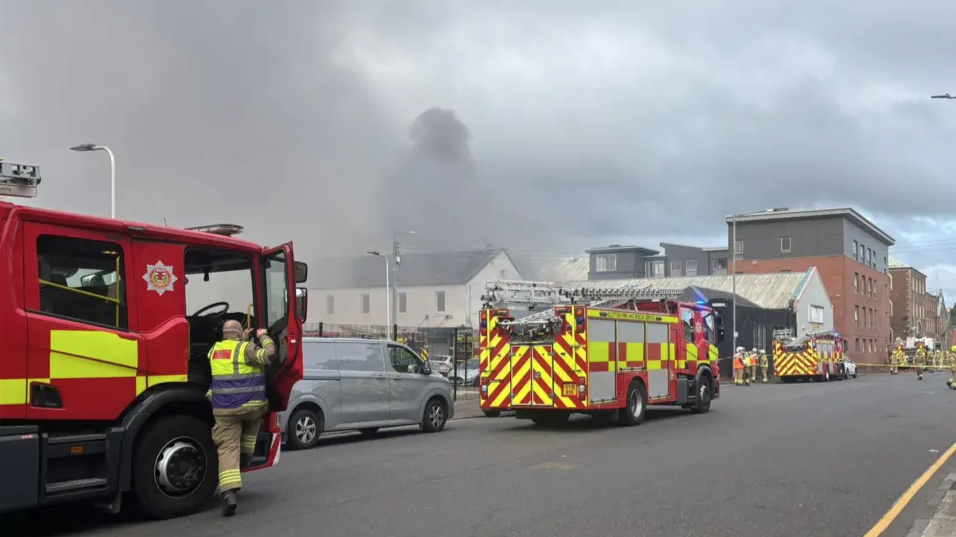 Three fire engines and several firefighters in the street next to the fire