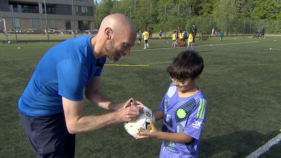 Luke Chadwick, in blue T-shirt, signs a football for a child wearing a mauve Manchester United shirt.