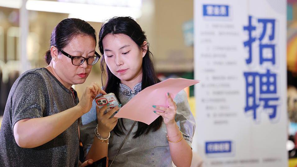 The picture shows two women reading instructions on a mobile phone while at a job fair in China's Lianyungang City.