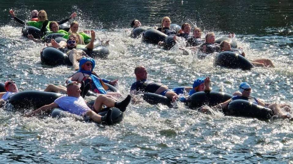 Teams of six in inflatable rings, which are linked together like a snake, racing in Castletown Harbour. The competitors are using their arms to paddle, which is creating lots of white splash.