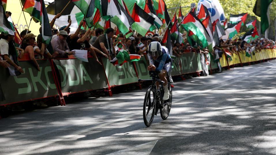 Spectators holding Palestinian flags line the route of a cycling race as a rider for the Israel Premier Tech teams rolls by