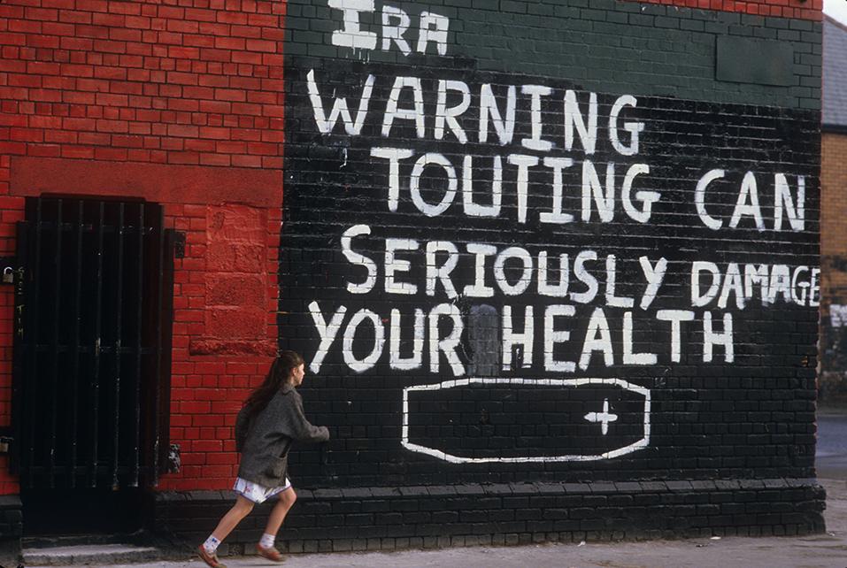 1980s pic of wall with graffiti: "IRA warning touting can seriously damage your health"