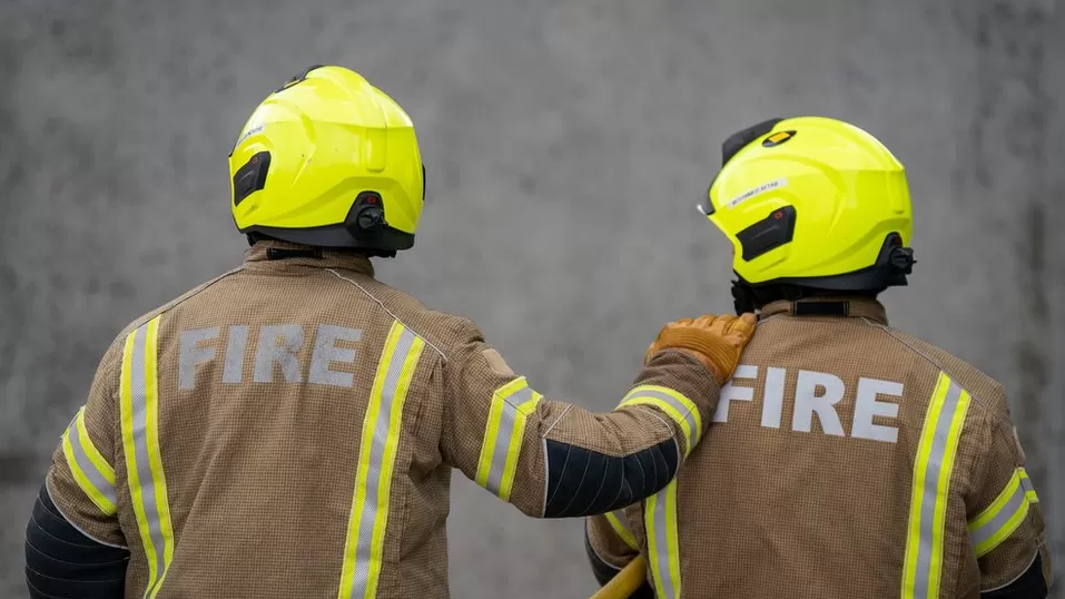 A stock image of two fire fighters wearing their safety equipment, one of them has their hand on the other's shoulder.