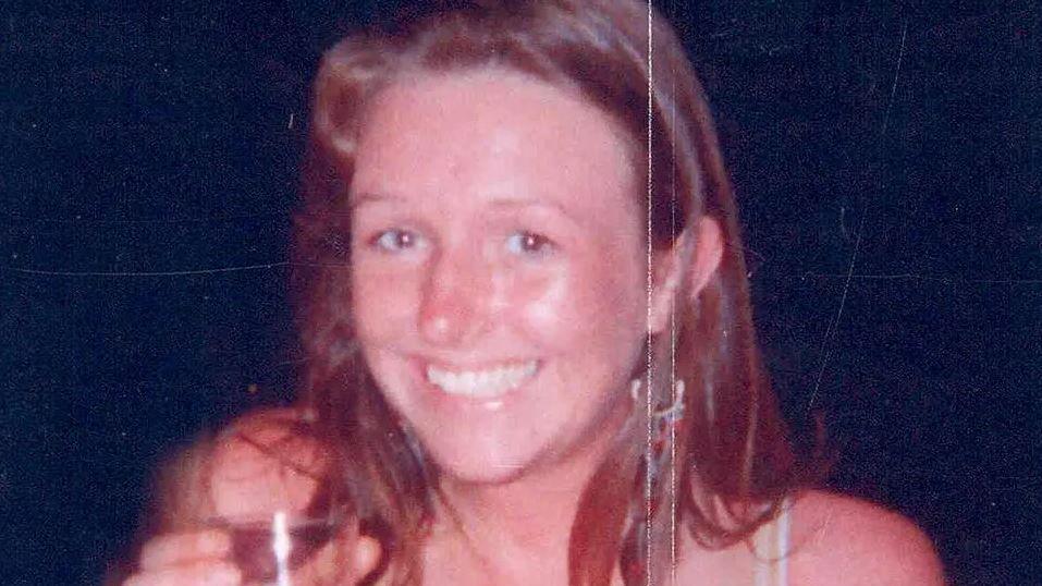 Head and shoulders image of Lucy Hargreaves smiling at the camera and holding a drink against a black background.