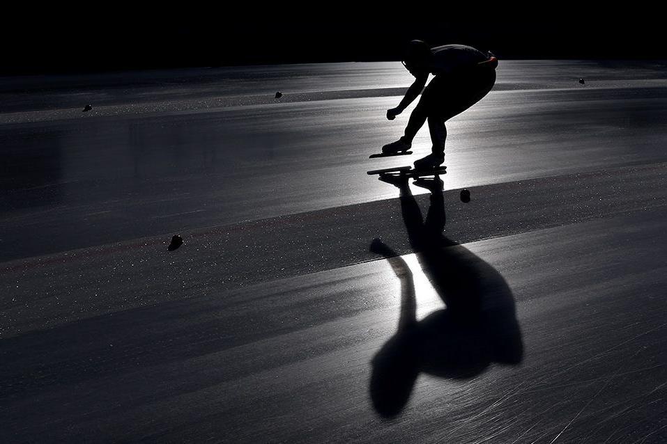 A speed skater glides in silhouette on an ice rink, with long shadows cast on the smooth surface