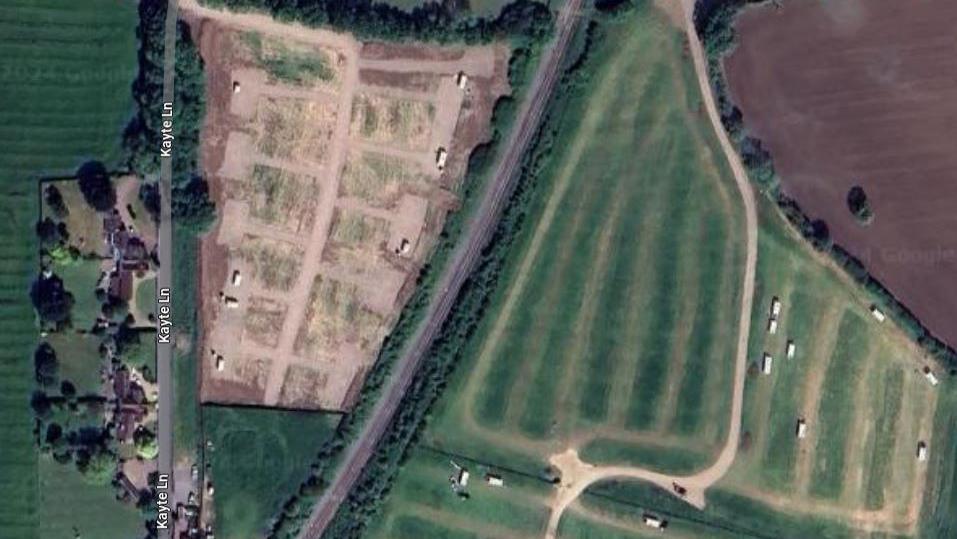 Google Maps aerial view showing a field with white rectangles, which are caravans