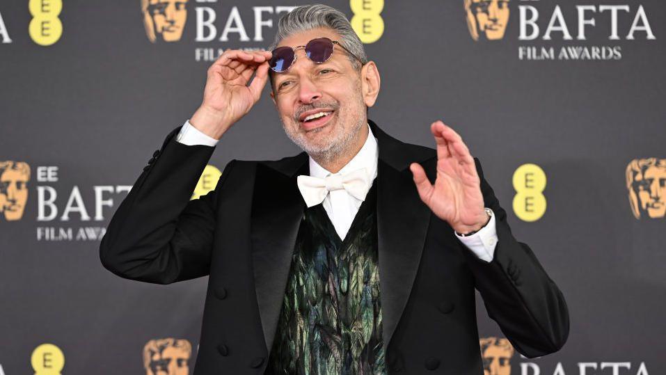 Jeff Goldblum in a feather waistcoat of greens and purples and a black tuxedo and white bow tie