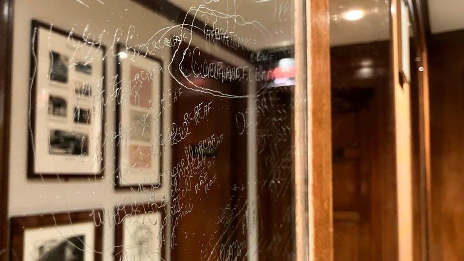 A mirror with names and messages carved into it from a side view.