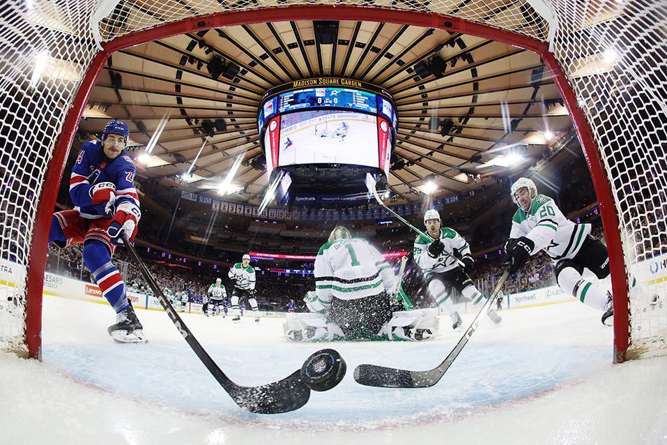 An ice hockey puck slides toward the goal near the net as two players try to get a decisive touch with hockey sticks