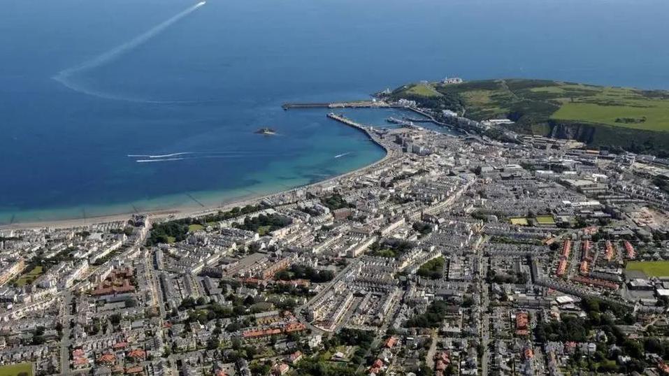 An aerial view of Douglas showing a large area that is built up with a green headland in the background and the Douglas Bay stretching out into the distance.