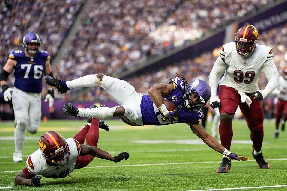 Aaron Jones of the Minnesota Vikings dives forward with the ball while a Washington Commanders player attempts a tackle in mid-air