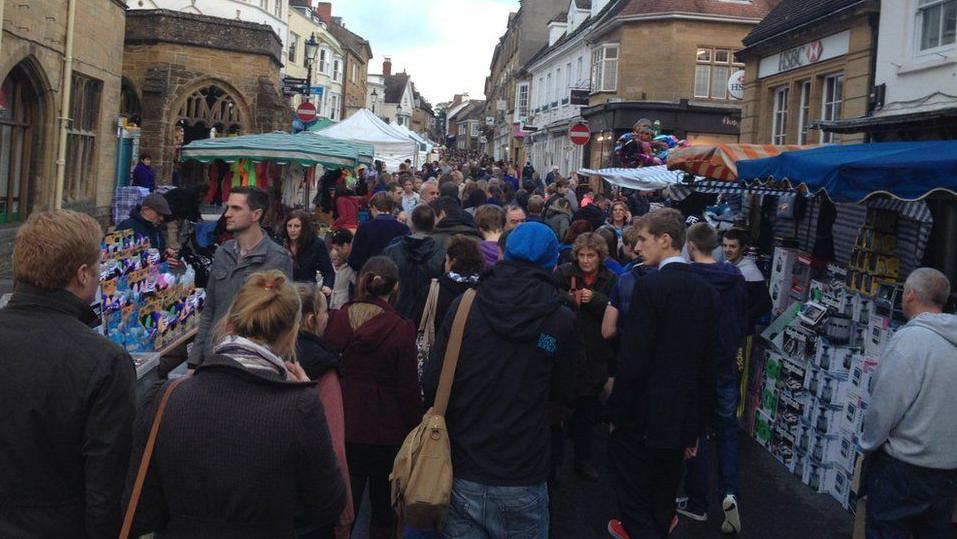 Throngs of people fill the street, with market stalls on either side.