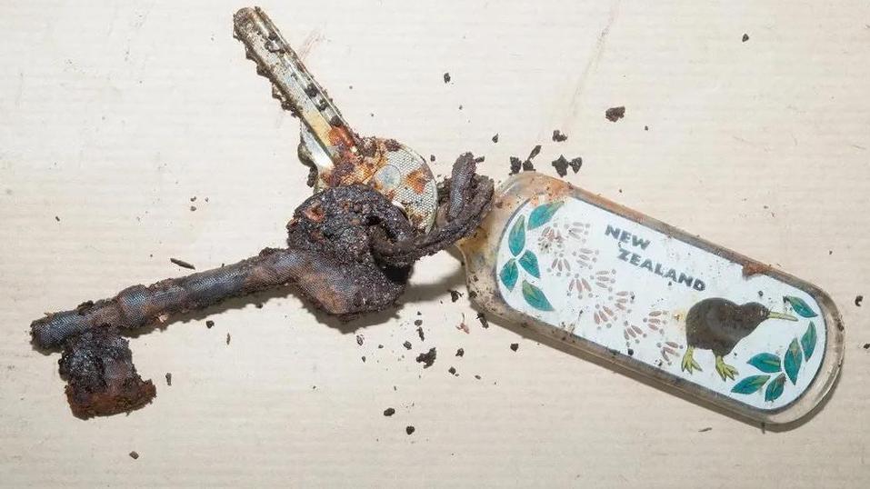 Two rusty keys can be seen with a key ring featuring the wording 'New Zealand' and a kiwi bird.