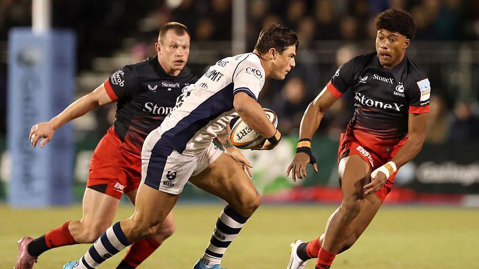 Louis Rees-Zammit (centre) runs with the ball as two Saracens players surround him
