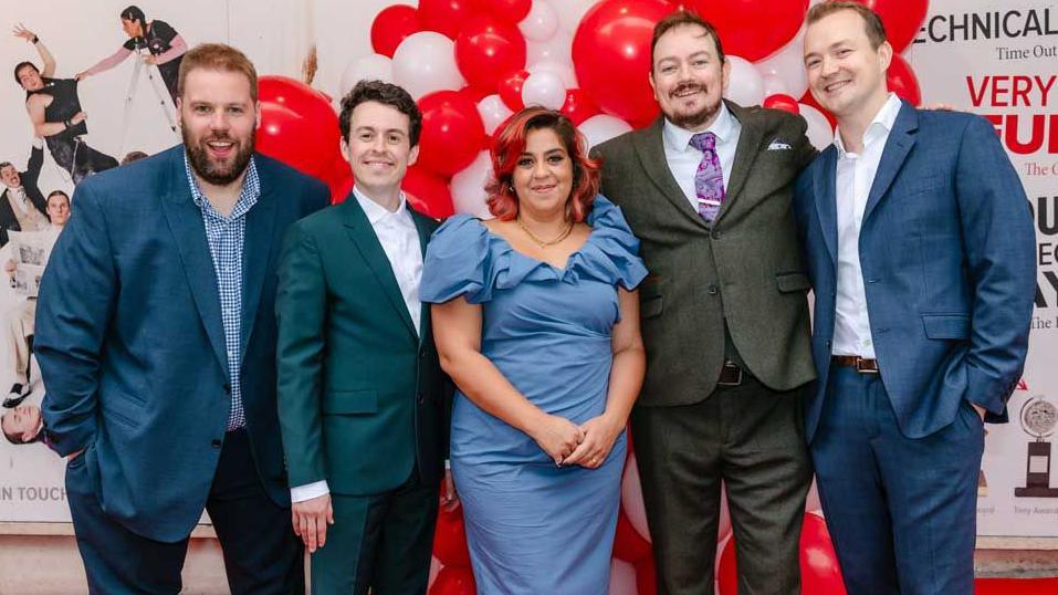 The original cast of The Play That Goes Wrong celebrating the 10th anniversary of the show in the West End on a red carpet in front of red and white balloons and a board advertising the play