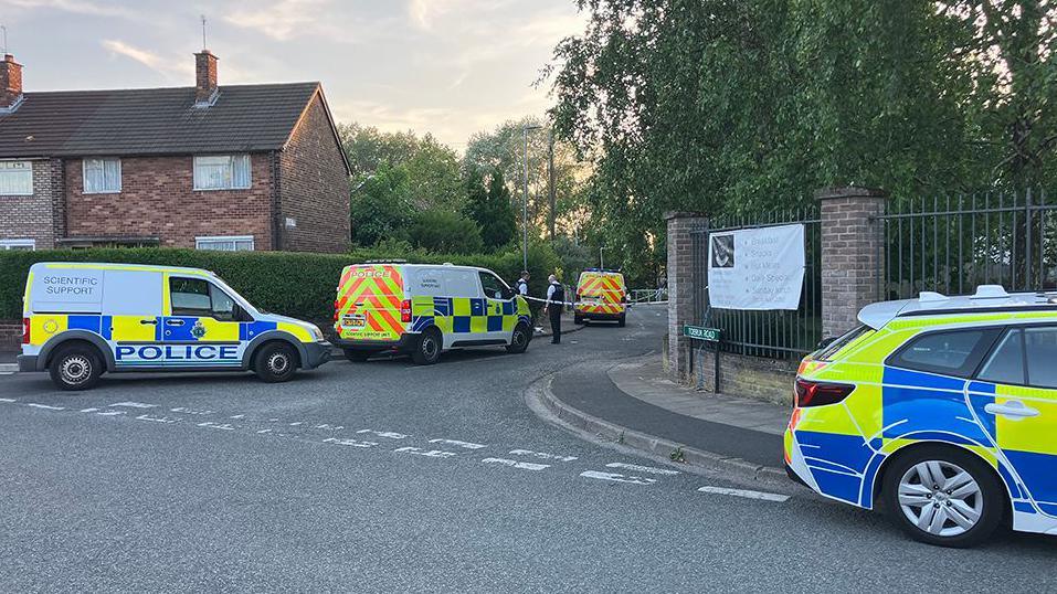 Merseyside Police officers and vehicles inside a cordon following an incident around the Tobruck Road area in Huyton on a sunny evening.