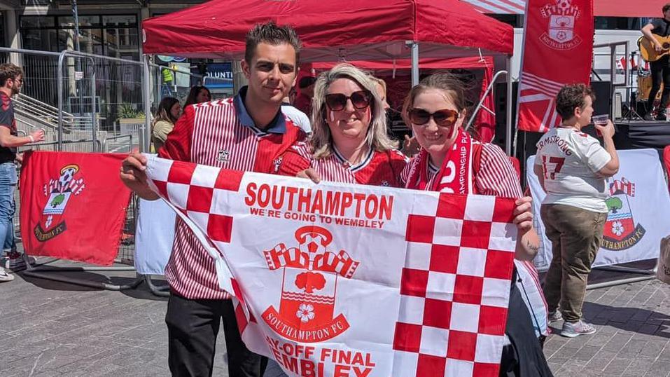 three people stand with saints flag