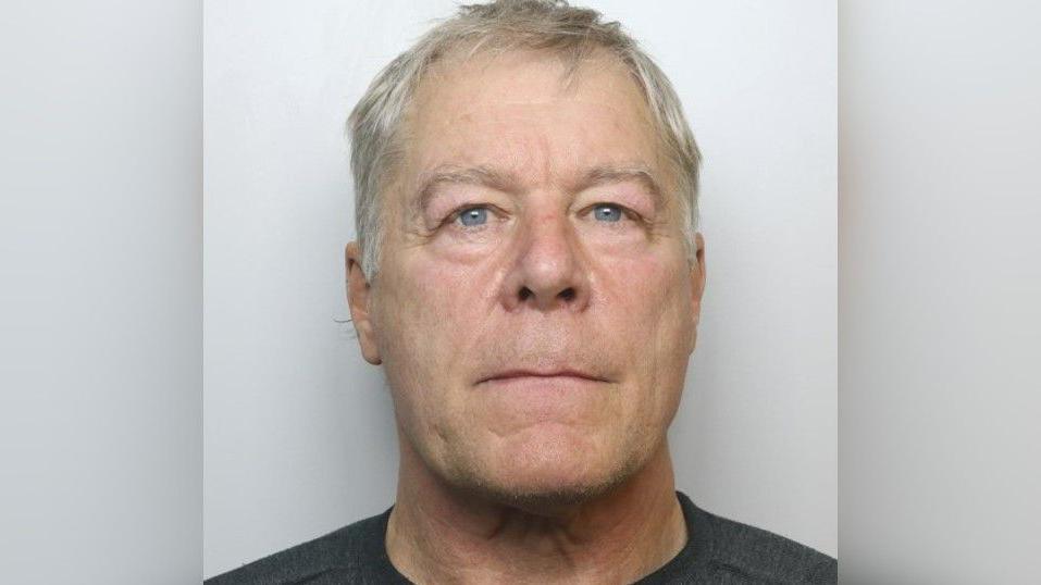 Headshot of a man with grey hair and blue eyes. He is wearing a black T-shirt.