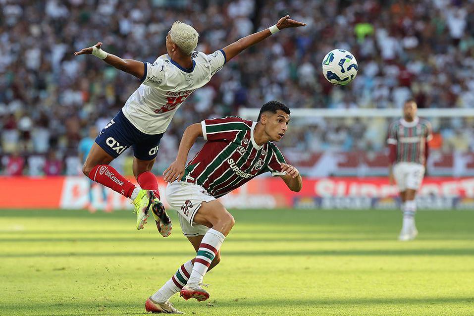 Erick Pulga leaps dramatically high with his arms outstretched while Kevin Serna bends forward attempting an interception
