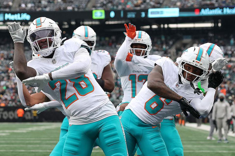 Jaylen Waddle and fellow Miami Dolphins players celebrate a touchdown on the football field after a successful play, with arms raised in in a choreographed dance move