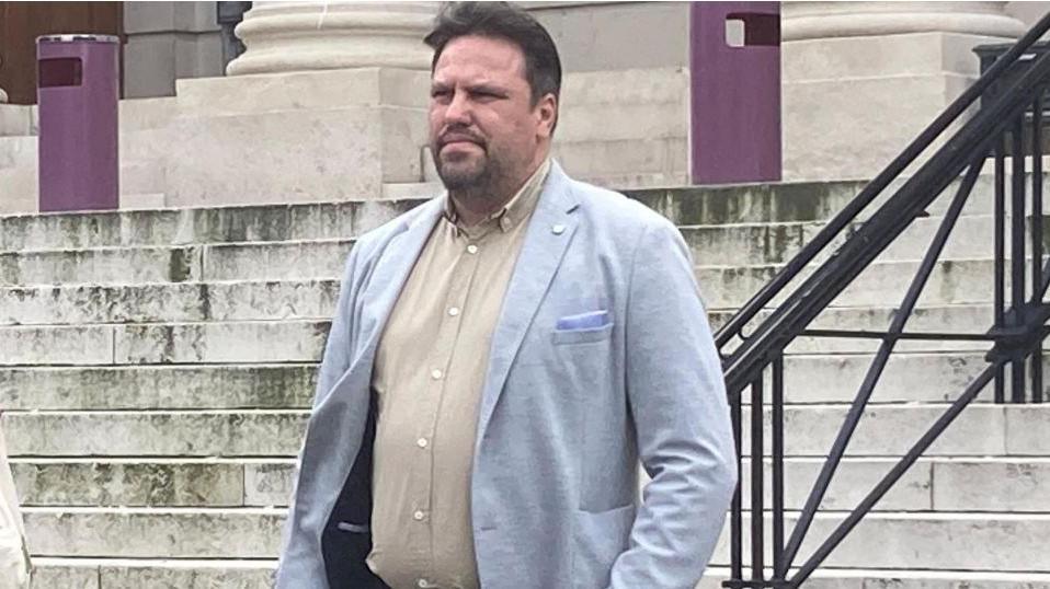 Vasile Barbu in a blue jacket outside court. He has a cream shirt and, and short dark hair and a goatee.