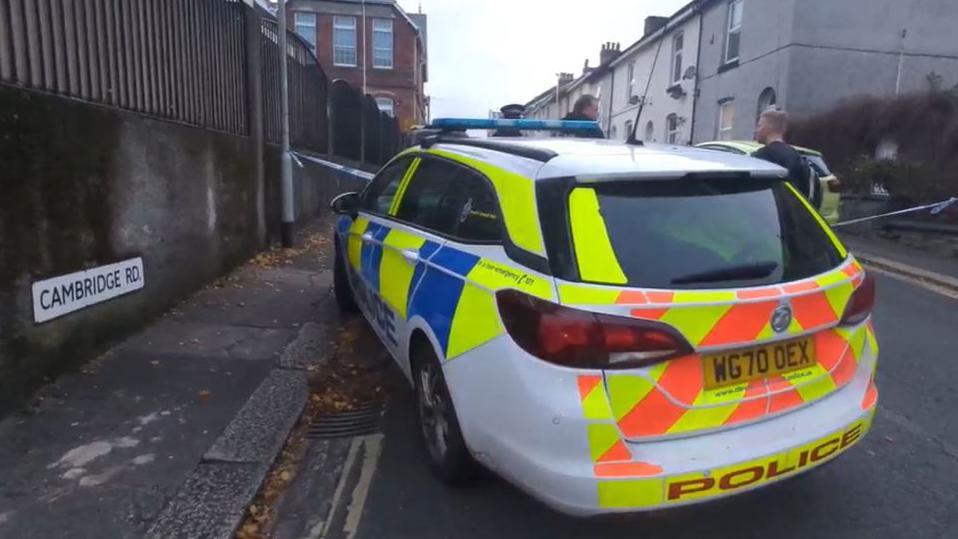 A police car and three police officers stand by a cordon on Cambridge Road in Plymouth following reports of a stabbing which led to the death of a 36-year-old man.