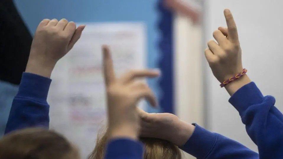 A group of children with their hands in the air. Their sleeves are all blue.