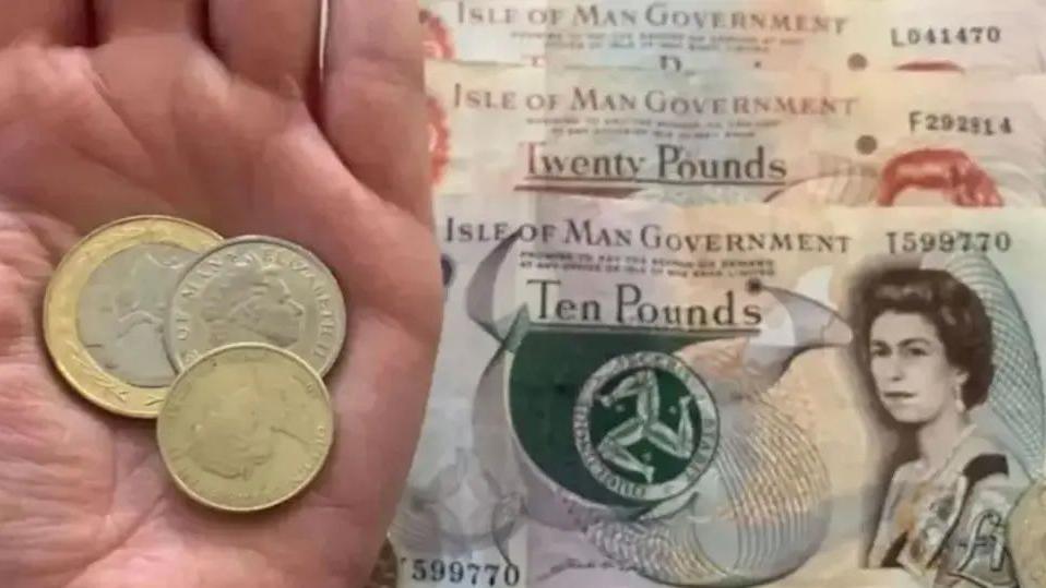 Two one poun and one two pound coins in someone's hand with ten and twenty pound notes laid out on a table beneath.